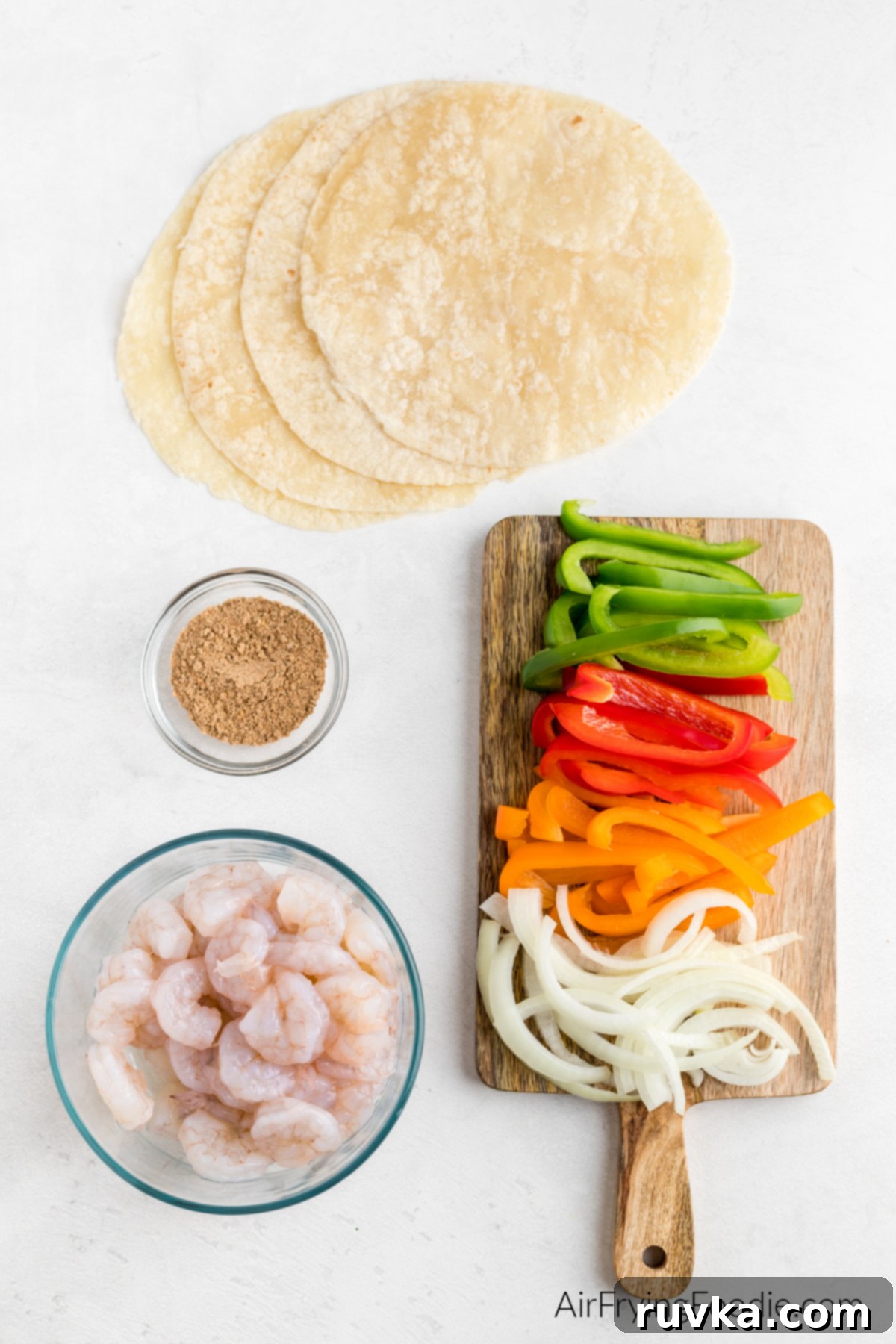 Effortless Air Fryer Shrimp Fajitas 3 Shrimp, sliced onion and bell peppers on a board, seasoning, and tortillas on a table ready to be prepared.