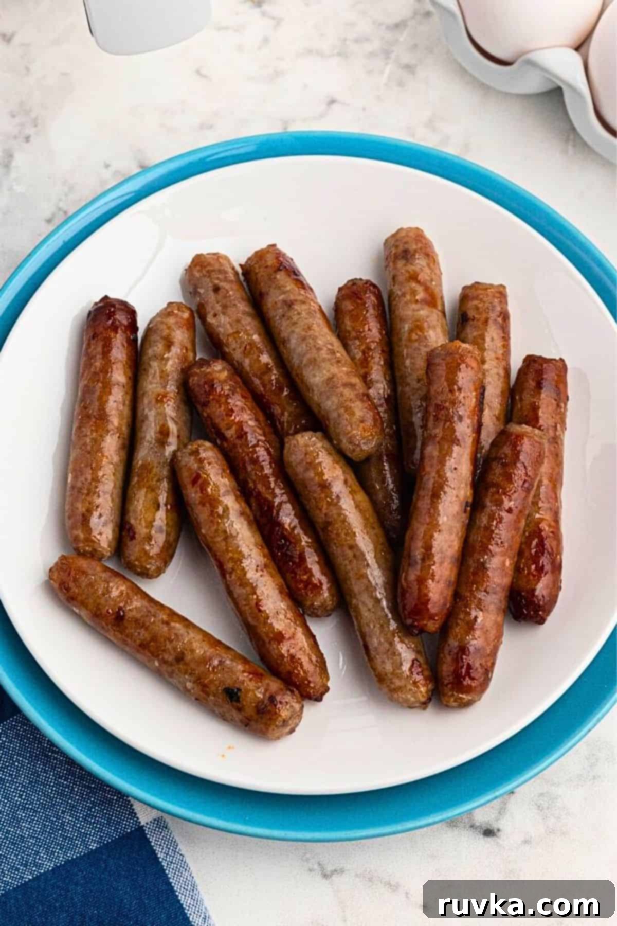 Crispy Air Fryer Sausage Links 2 White plate filled with crispy, golden brown, cooked sausage links, on a marble table in front of an air fryer.