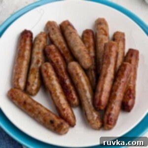 Crispy Air Fryer Sausage Links 7 White plate filled with crispy, golden brown, cooked sausage links, on a marble table in front of an air fryer.