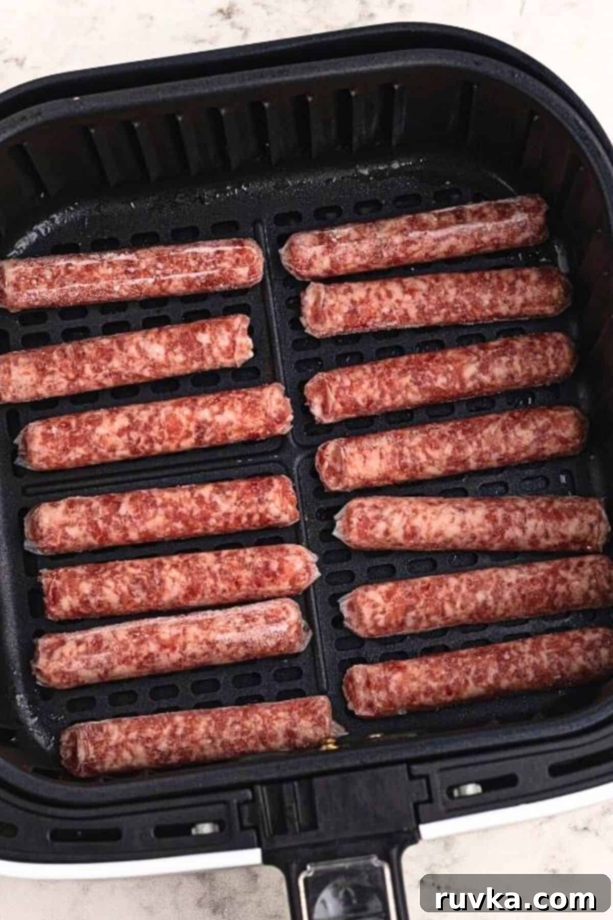 Crispy Air Fryer Sausage Links 4 Uncooked sausage links placed side by side in the air fryer basket.