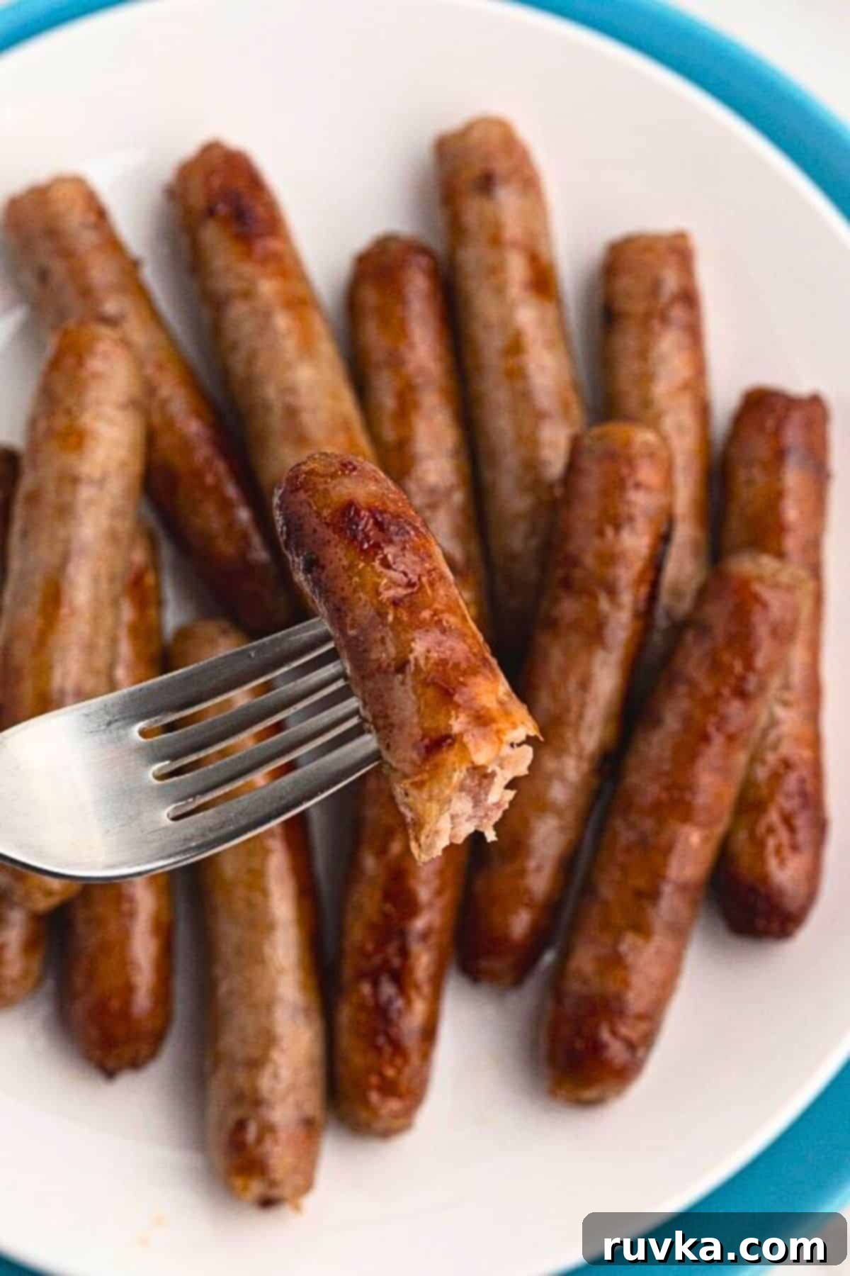 Crispy Air Fryer Sausage Links 6 Golden sausage links cooked and stacked on a white plate, with one link on a fork.