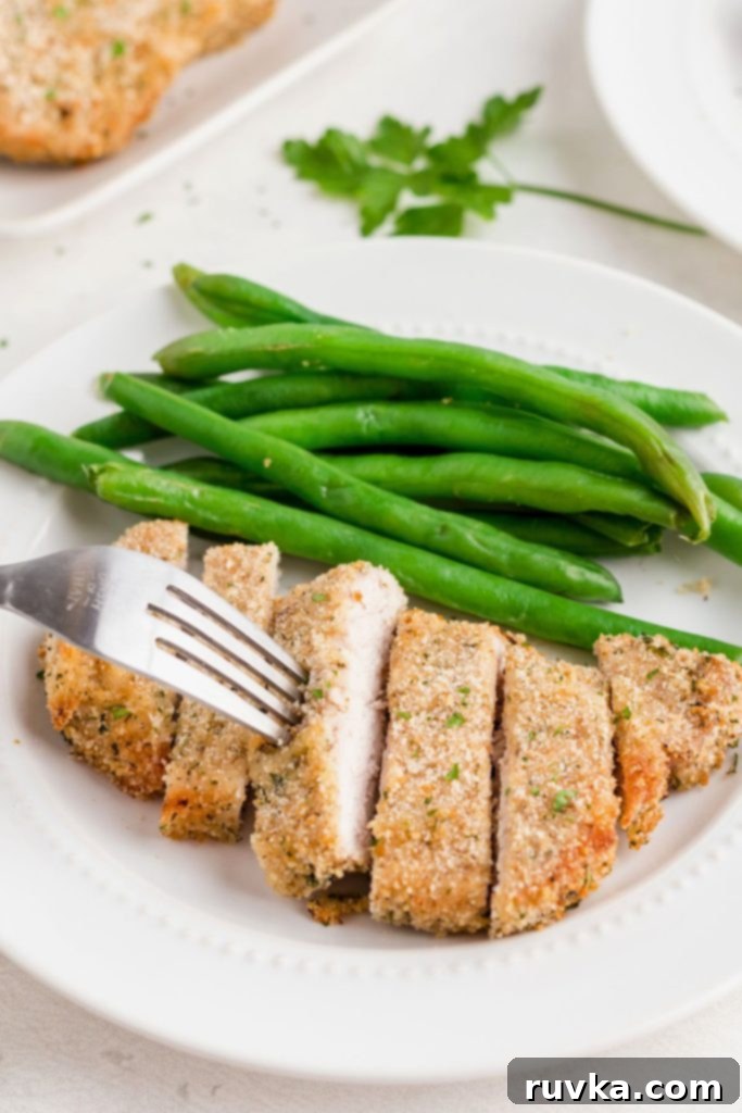 Golden Crispy Air Fryer Pork Chops 8 Breaded pork chop on a white plate, cut into slices and served with green beans.