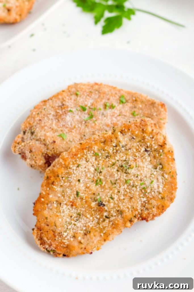 Golden Crispy Air Fryer Pork Chops 9 Golden brown breaded and seasoned pork chops on a white plate.