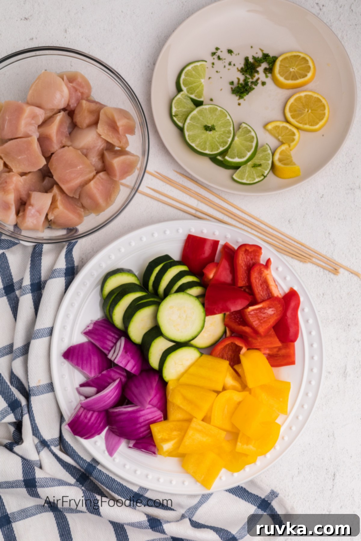 Easy Air Fryer Chicken Kabobs 3 Chopped vegetables on a plate. wooden skewers, chicken bites, and lime and lemons and a plate.