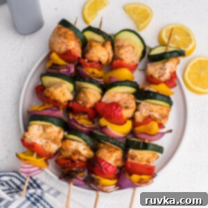 Easy Air Fryer Chicken Kabobs 9 chicken kabobs made in the air fryer with lemon slices and served on a white plate.