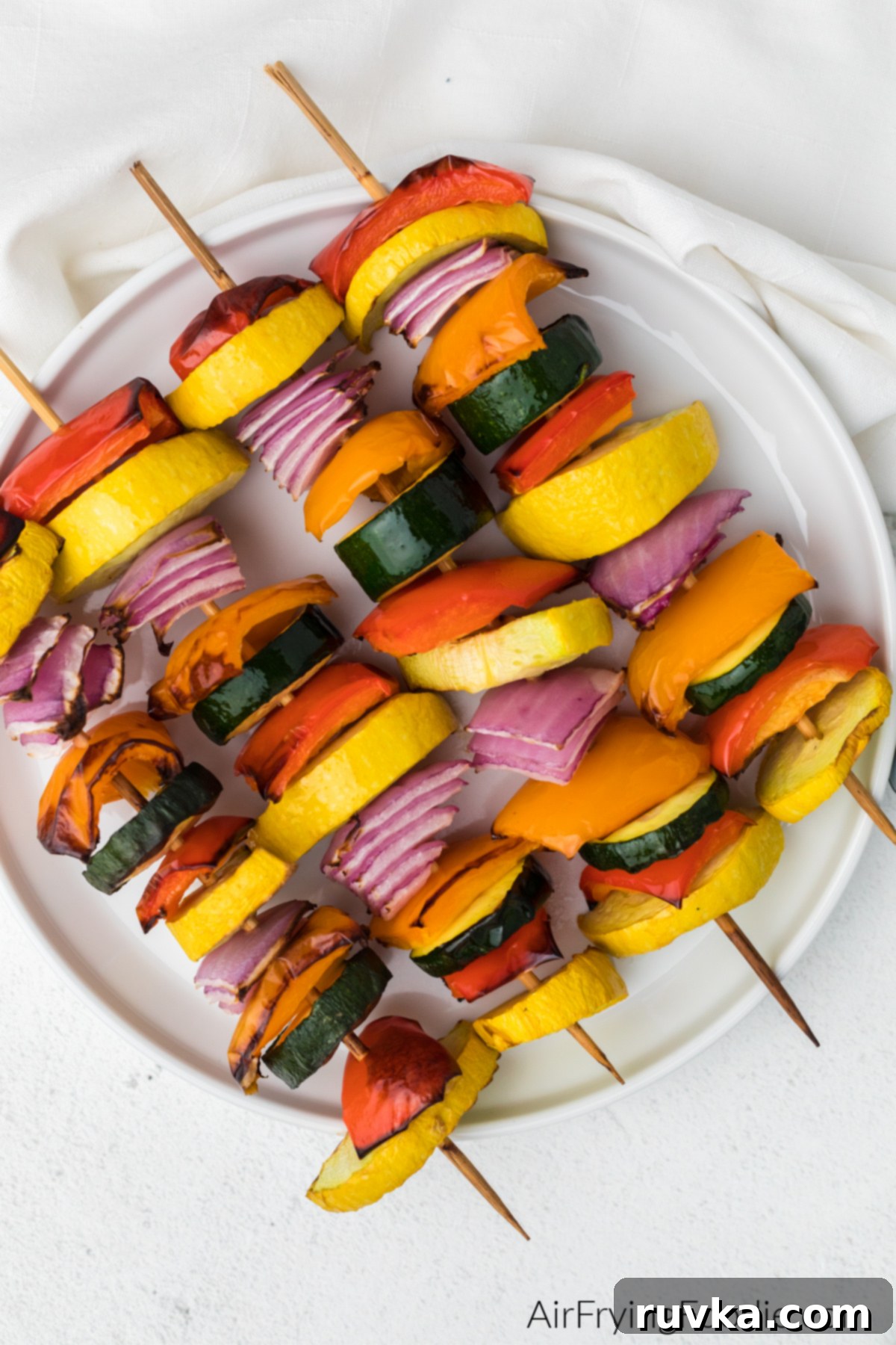 Crispy Air Fryer Vegetable Skewers 8 Perfectly cooked vegetable kabobs, featuring zucchini, bell peppers, and onion, beautifully presented on a white plate after being air fried.