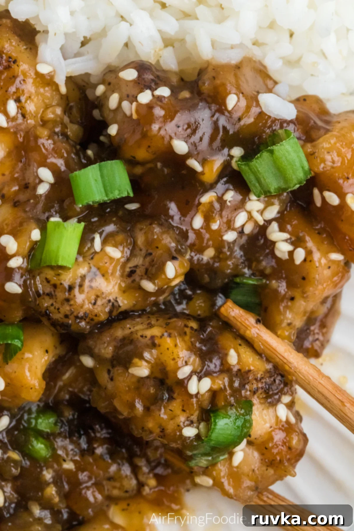Sticky Sweet Air Fryer Teriyaki Chicken 11 Close up photo of air fryer Teriyaki chicken topped with sesame seeds and green onions and served with chopsticks for eating.