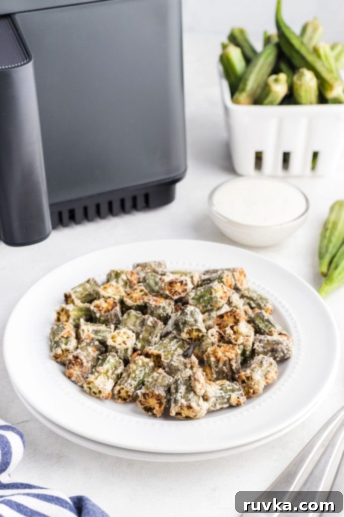 Crispy Air Fryer Okra 2 Golden fried okra in a white shallow plate in front of an air fryer.