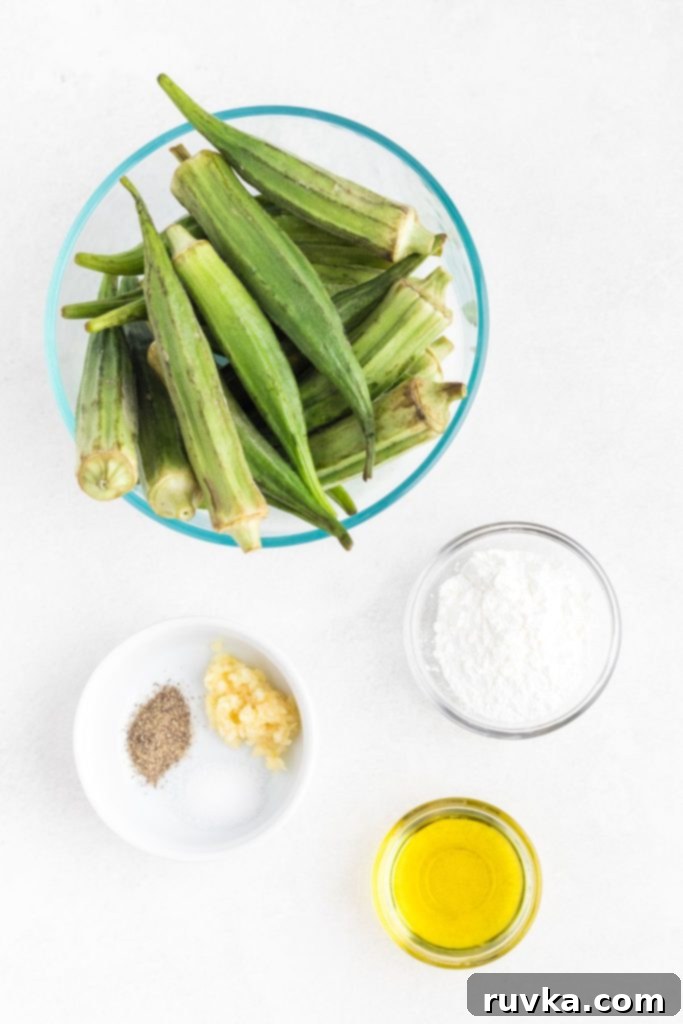 Crispy Air Fryer Okra 3 Uncooked okra, olive oil, garlic, seasonings, and cornstarch, measured in bowls on a white marble table.