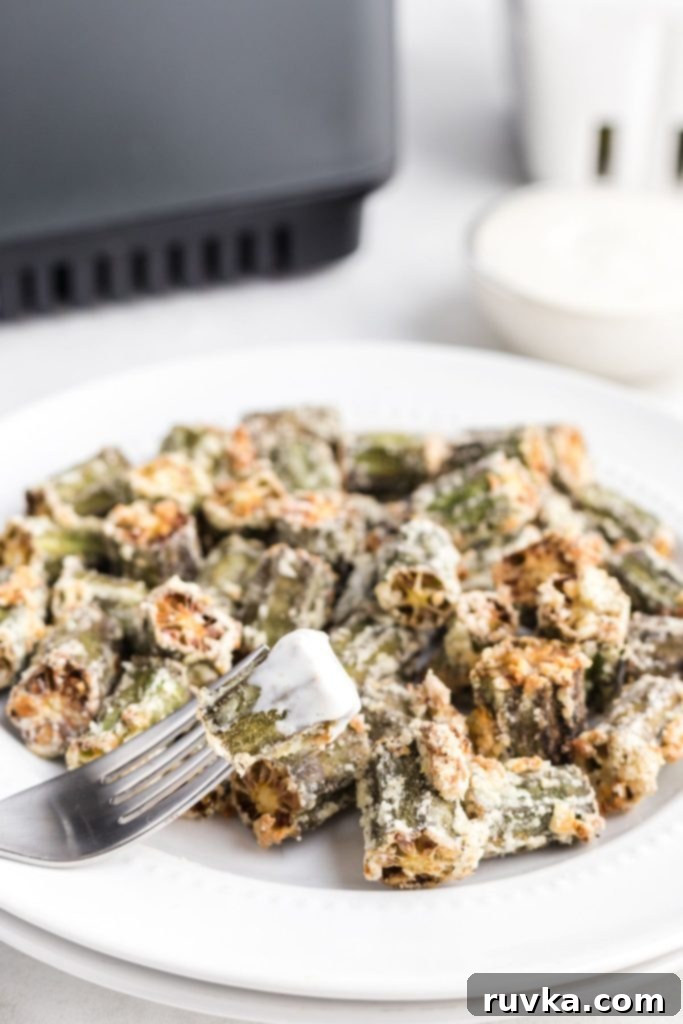 Crispy Air Fryer Okra 9 Golden okra pieces on a white plate with one piece dipped in ranch dressing on a fork.