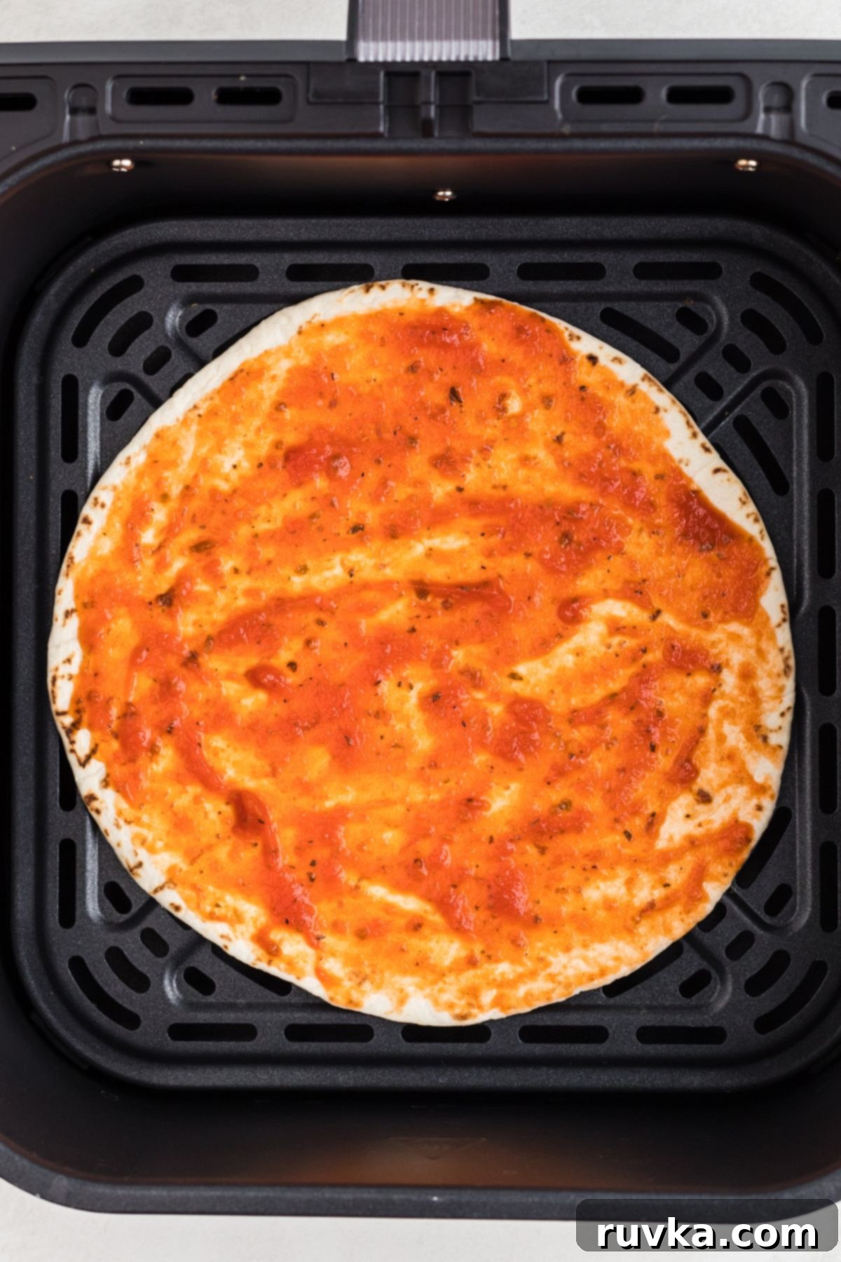 Crispy Air Fryer Tortilla Pizzas 4 Tortilla in the air fryer basket with pizza sauce spread on top.