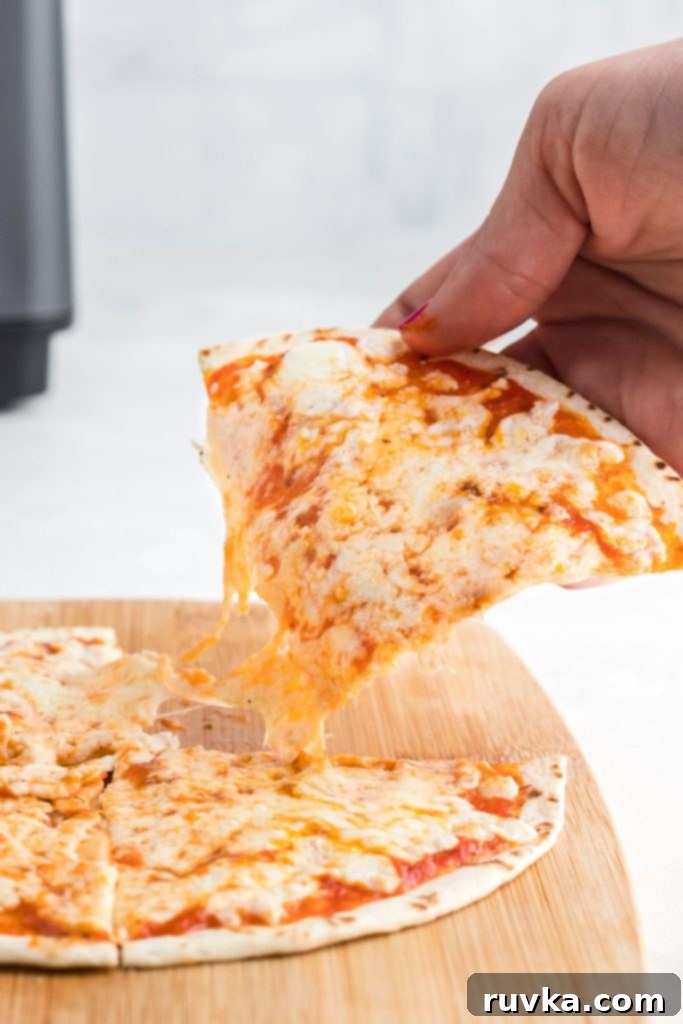 Crispy Air Fryer Tortilla Pizzas 8 Cheesy tortilla pizza being pulled off of cutting board.