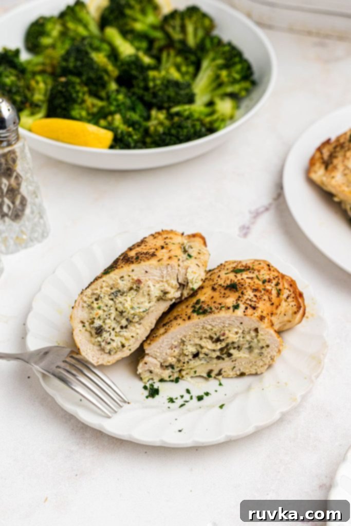 Crispy Air Fryer Stuffed Chicken 9 Golden cooked chicken on a small white plate in front of a bowl of broccoli on a marble table.