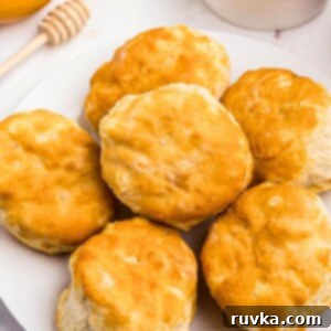 Easy Air Fryer Frozen Biscuits 8 Golden biscuits on a white small plate in front of butter and honey.