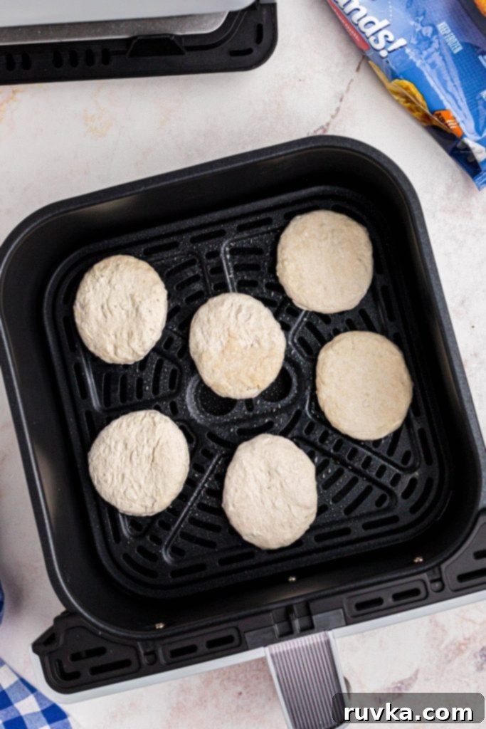 Easy Air Fryer Frozen Biscuits 4 Frozen biscuits in the air fryer basket on a white marble table.
