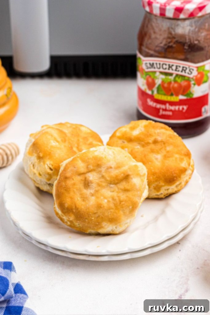 Easy Air Fryer Frozen Biscuits 6 Golden fluffy biscuits on a small white plate in front of jam.