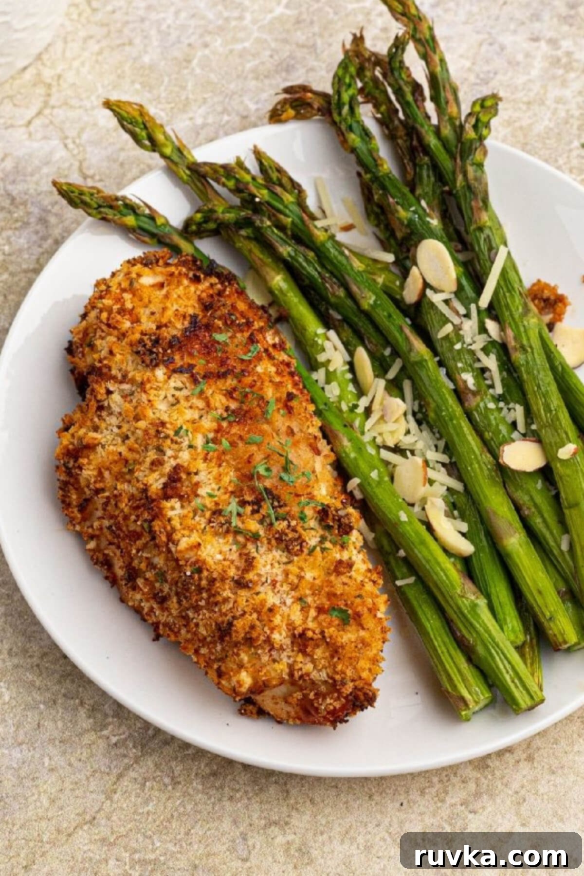 Delicious Air Fryer Chicken Recipes Made Easy 12 Golden brown air fryer Parmesan crusted chicken served on a white plate with a side of fresh asparagus.