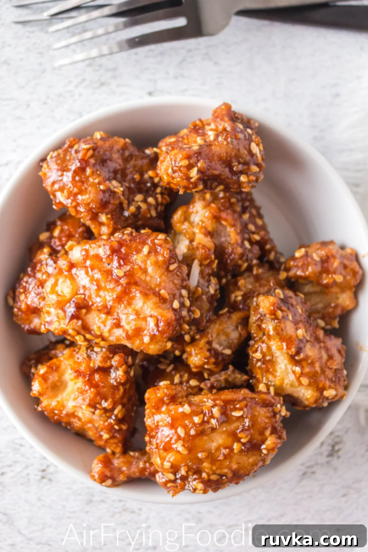 Delicious Air Fryer Chicken Recipes Made Easy 21 Overhead shot of delectable air fryer sesame chicken, garnished with sesame seeds and green onions, served in a white bowl.