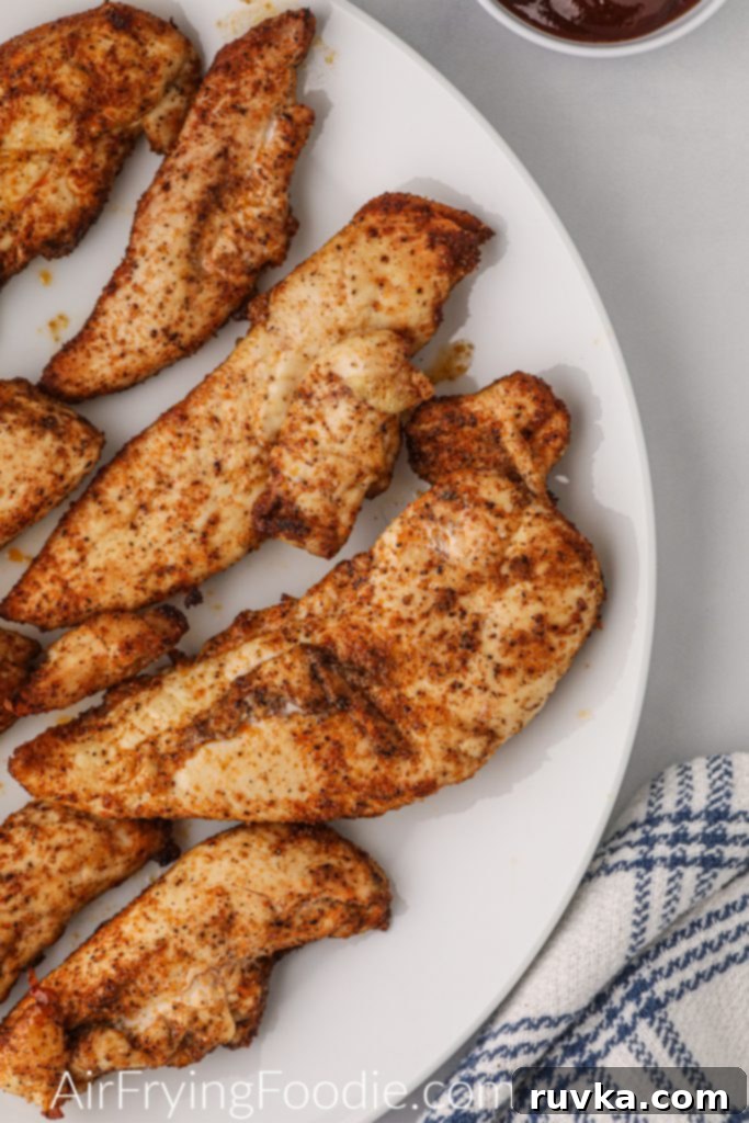 Delicious Air Fryer Chicken Recipes Made Easy 4 Naked air fryer chicken tenders, unbreaded and grilled, served on a white plate with a side of dipping sauce.