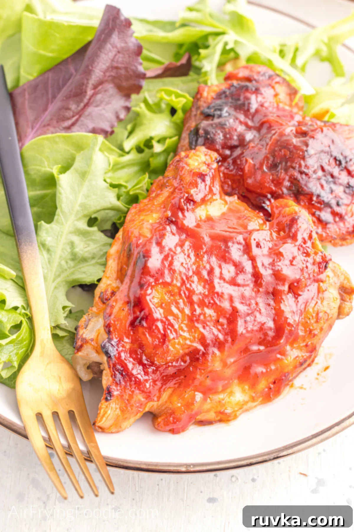 Delicious Air Fryer Chicken Recipes Made Easy 47 Air fried BBQ chicken thighs, perfectly sauced and tender, served on a plate with a fresh side salad and a fork.
