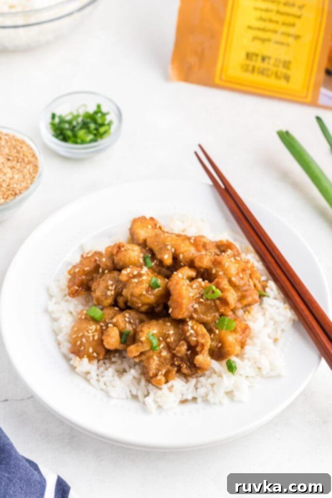 Trader Joes Orange Chicken in the Air Fryer 2 Golden orange chicken on white rice in a white bowl with chopsticks on the side of the bowl.