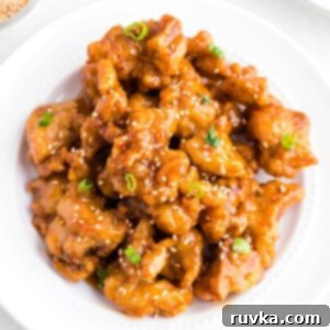 Trader Joes Orange Chicken in the Air Fryer 9 Golden crispy chicken pieces coated in an orange sauce served in a white bowl.