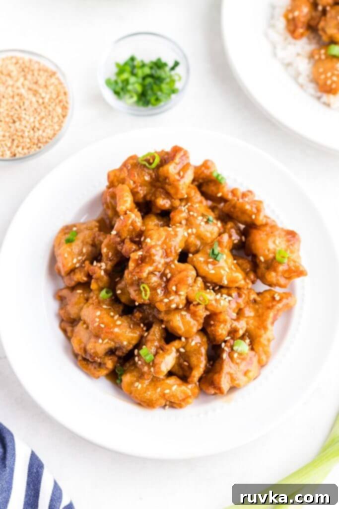 Trader Joes Orange Chicken in the Air Fryer 3 Golden orange chicken pieces in a white bowl topped with sesame seeds and chopped green onion.