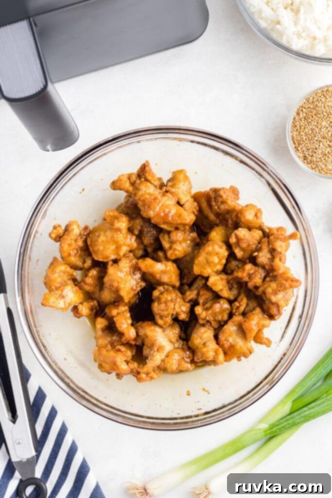 Trader Joes Orange Chicken in the Air Fryer 6 Crispy cooked pieces of chicken in a clear glass bowl being mixed with orange sauce.