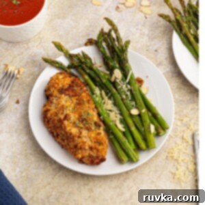 Easy Air Fryer Dinners 15 Cooked parmesan crusted chicken served with green asparagus on a white plate.