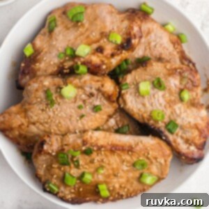 Easy Air Fryer Dinners 4 Juicy pork chops cooked and served in a white shallow bowl. Sprinkled with green onions and sesame seeds.