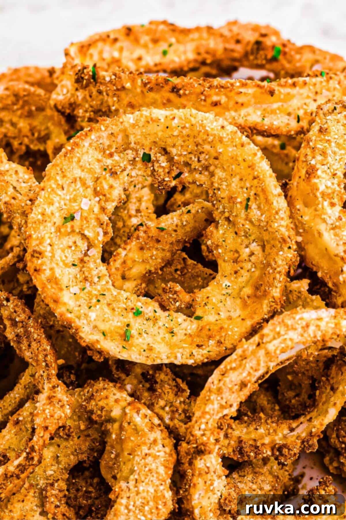 Mastering Air Fryer Leftovers for Crispy Results 14 Golden crispy battered onion rings stacked on a white plate.