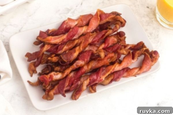 Air Fryer Twisted Bacon 2 Crispy bacon twisted into curls and stacked on a white rectangle plate. Orange juice in a glass on the side.