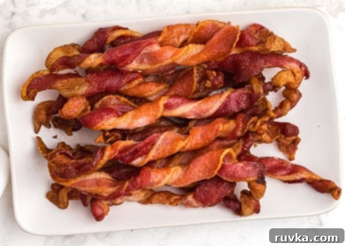 Air Fryer Twisted Bacon 3 crispy twisted bacon on a white rectangle plate, stacked on top of each other.