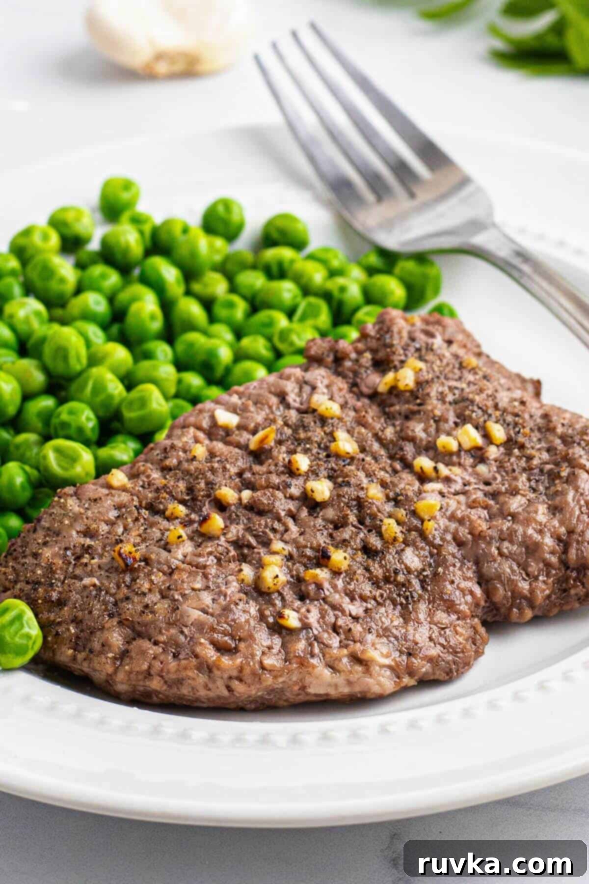 Easy Air Fryer Cube Steak 2 Juicy cube steak seasoned and served on a small white plate with green peas.