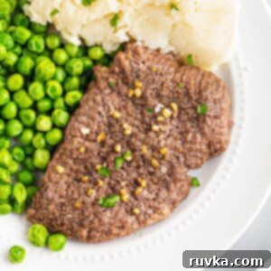 Easy Air Fryer Cube Steak 8 Juicy cube steak on a white plate served with green peas and mashed potatoes.