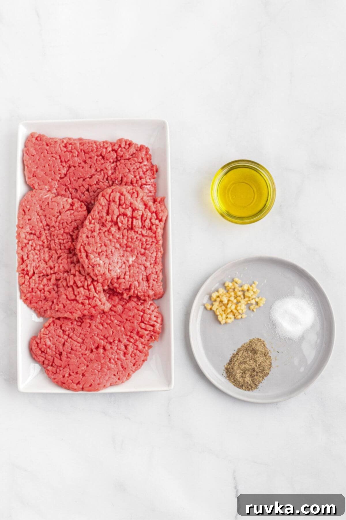 Easy Air Fryer Cube Steak 3 Cube steaks, olive oil, and seasonings measured out on white marble table.