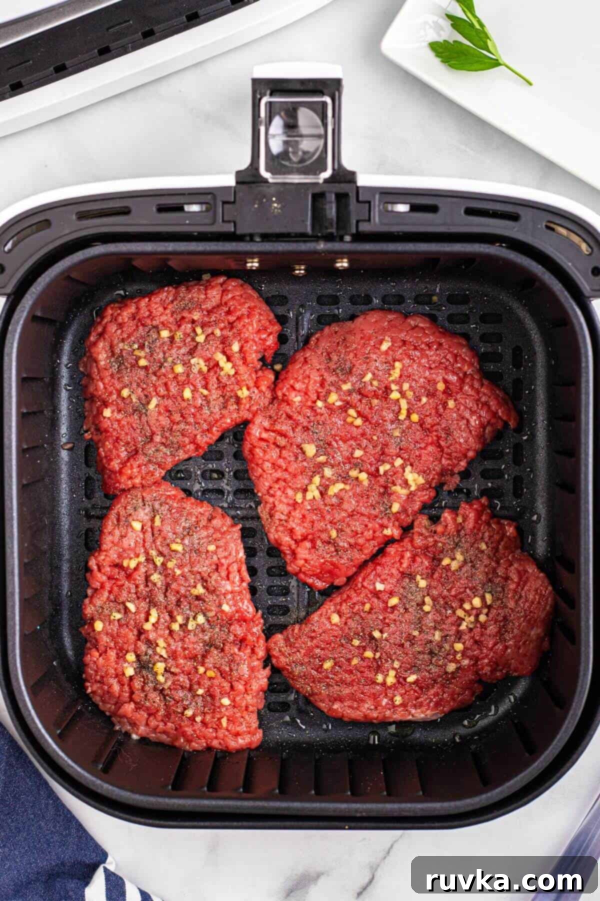 Easy Air Fryer Cube Steak 4 Uncooked cube steaks seasoned and placed in the air fryer basket.