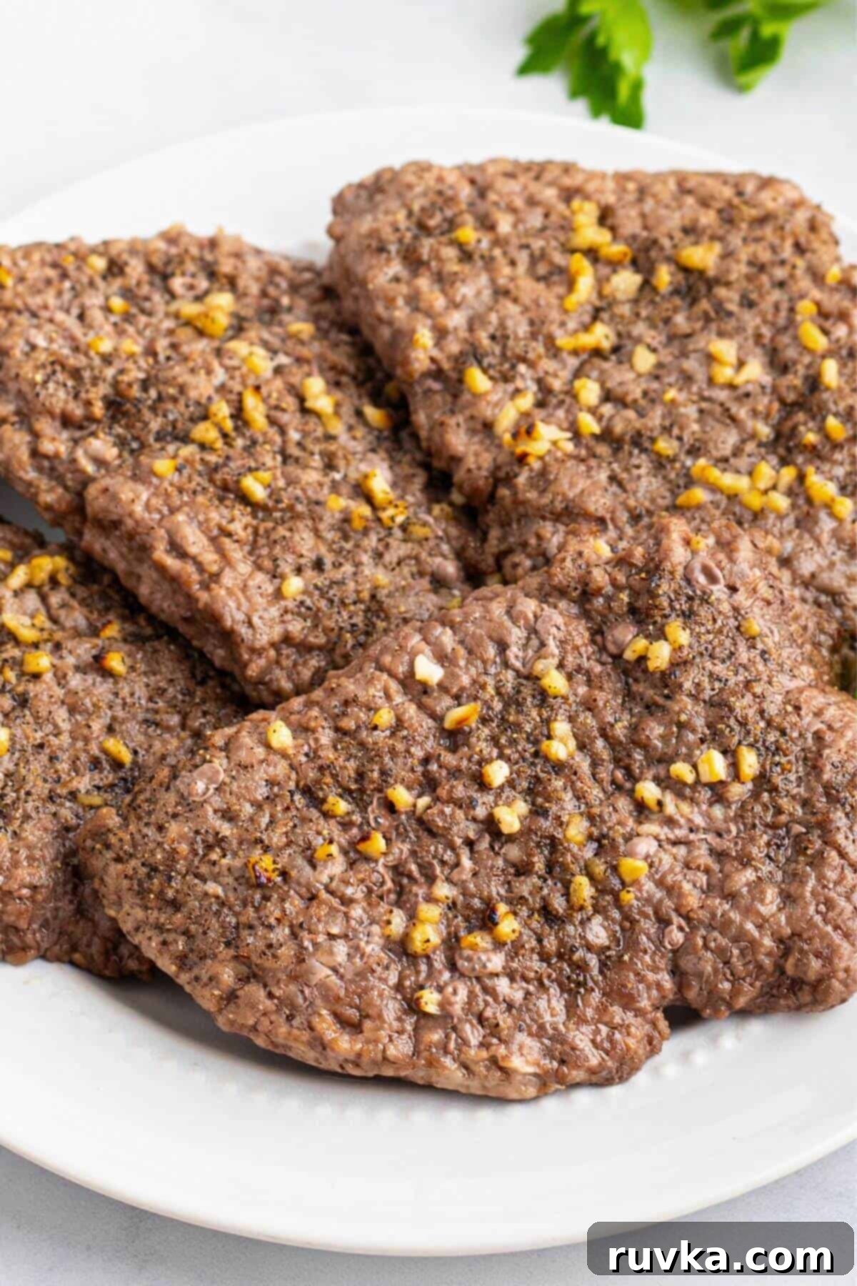 Easy Air Fryer Cube Steak 6 Juicy cube steaks seasoned with garlic, slat, and pepper, on a white plate.