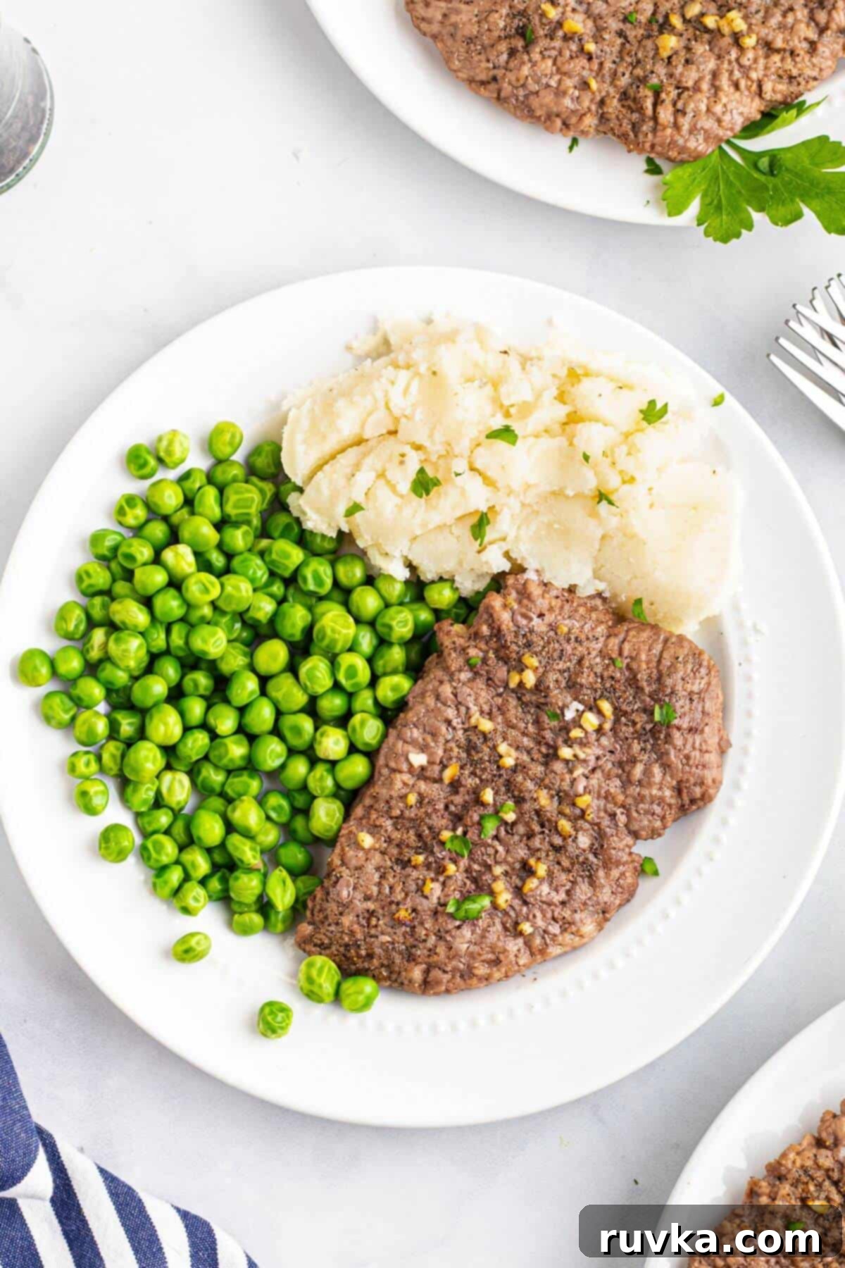 Easy Air Fryer Cube Steak 7 Juicy seasoned cube steak served on a white plate with green peas and mashed potatoes.