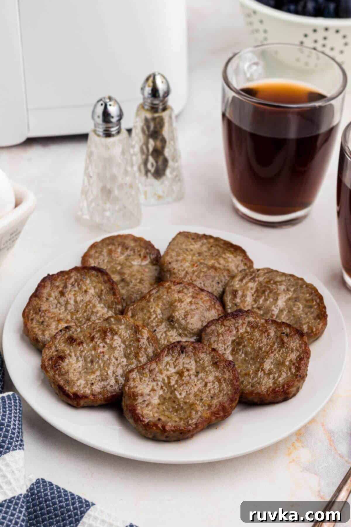 Perfect Air Fryer Sausage Patties 2 Brown juicy sausages on a white plate in front of an air fryer on a marble table.