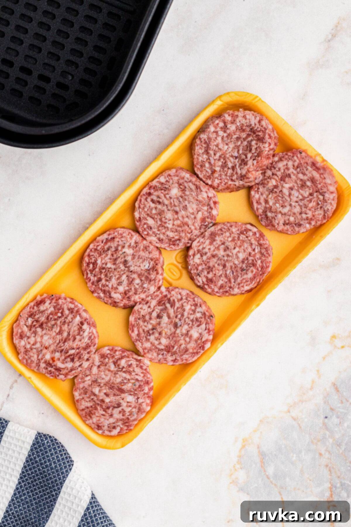 Perfect Air Fryer Sausage Patties 3 uncooked sausage patties in a yellow Styrofoam container on a marble table.