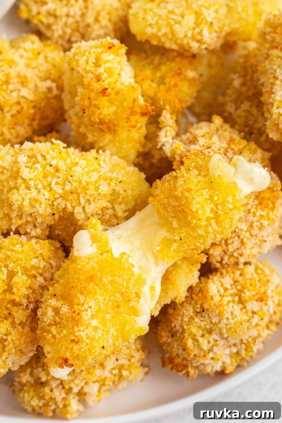 Crispy Air Fryer Cheese Curds 2 Golden breaded and fried melted cheese curds stacked on a white plate.
