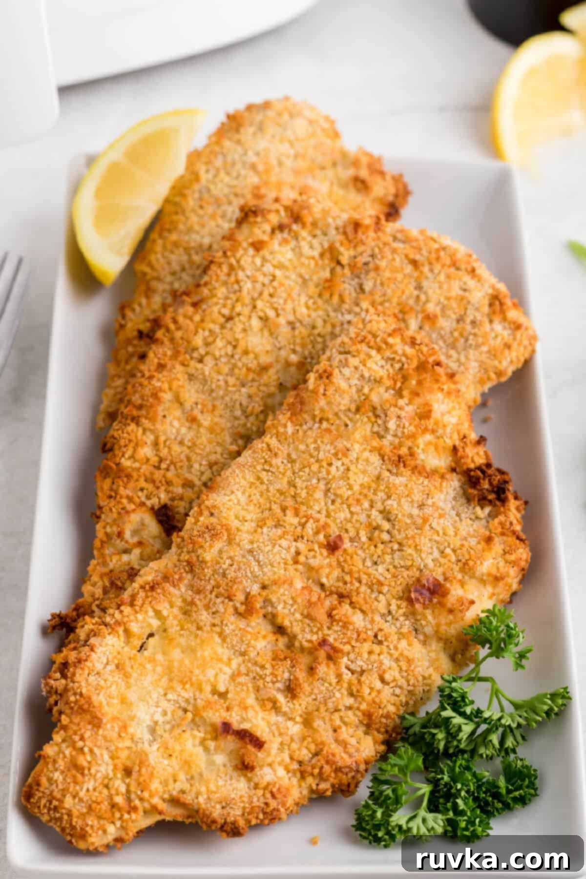 Air Fryer Reheat Crispy Fish Every Time 2 Crispy reheated fried fish in an air fryer, served golden brown on a white plate with a fresh slice of lemon.