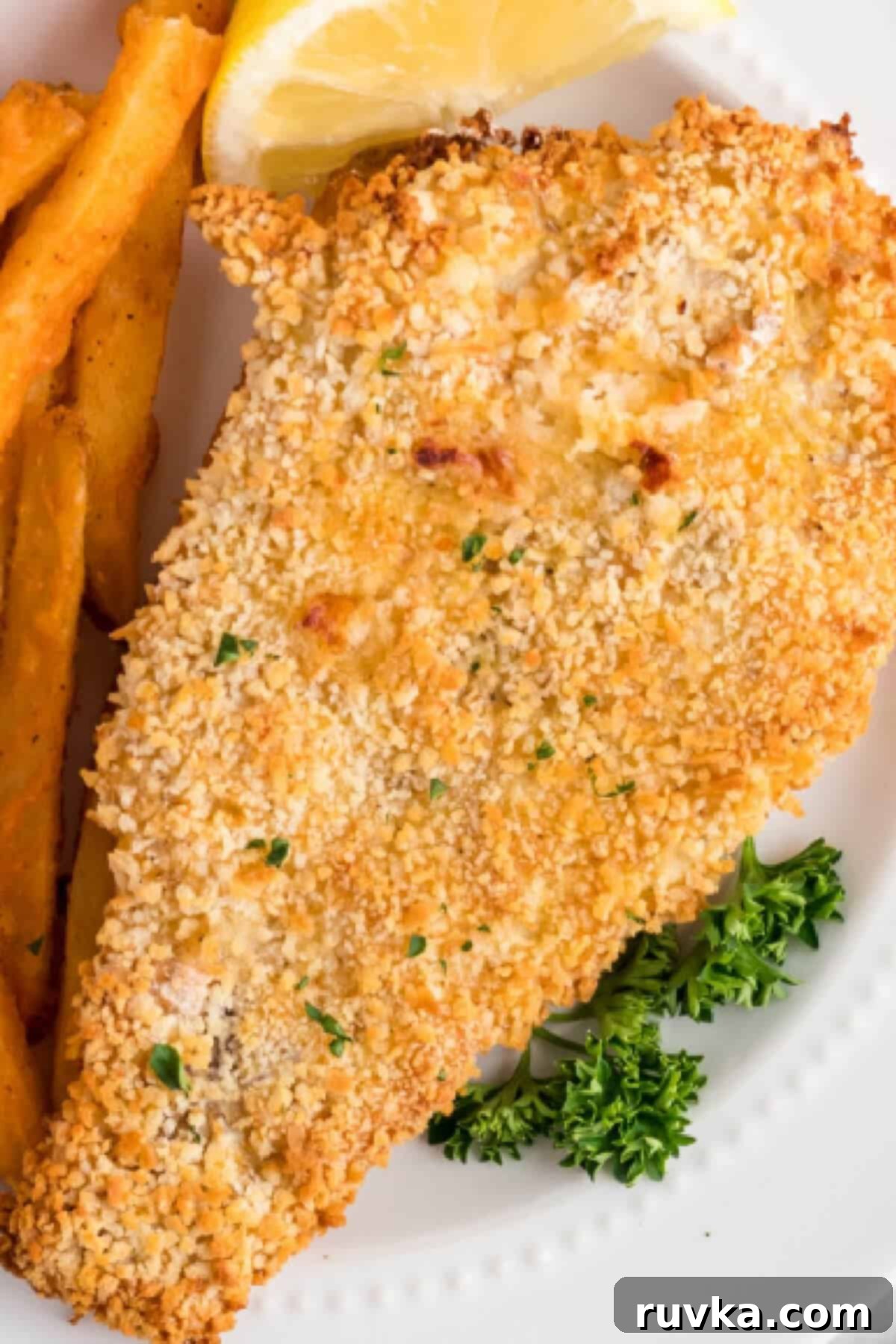 Air Fryer Reheat Crispy Fish Every Time 4 Golden brown fried fish, freshly reheated in an air fryer, served on a white plate alongside crispy french fries and a bright slice of lemon.