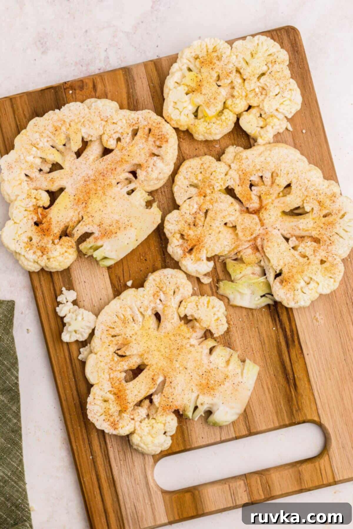 Crispy Air Fryer Cauliflower Steaks 6 Seasoned uncooked cauliflower steaks on a wooden cutting board before being air fried.