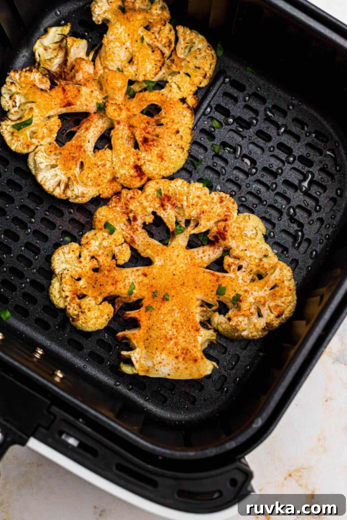 Crispy Air Fryer Cauliflower Steaks 7 Golden crispy seasoned cauliflower steaks in the air fryer basket after being cooked.