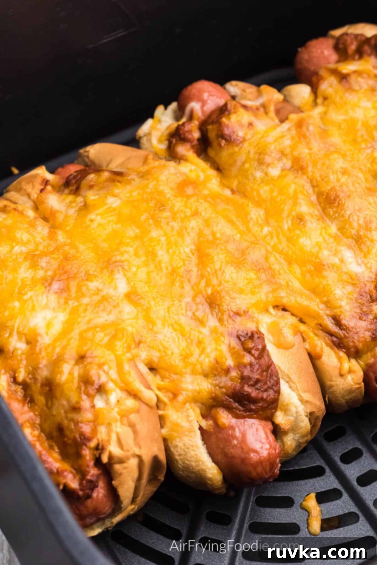 Crispy Air Fryer Chili Cheese Dogs 2 Chili cheese dogs in the basket of the air fryer, ready to be served, showcasing golden buns, melted cheese, and rich chili.