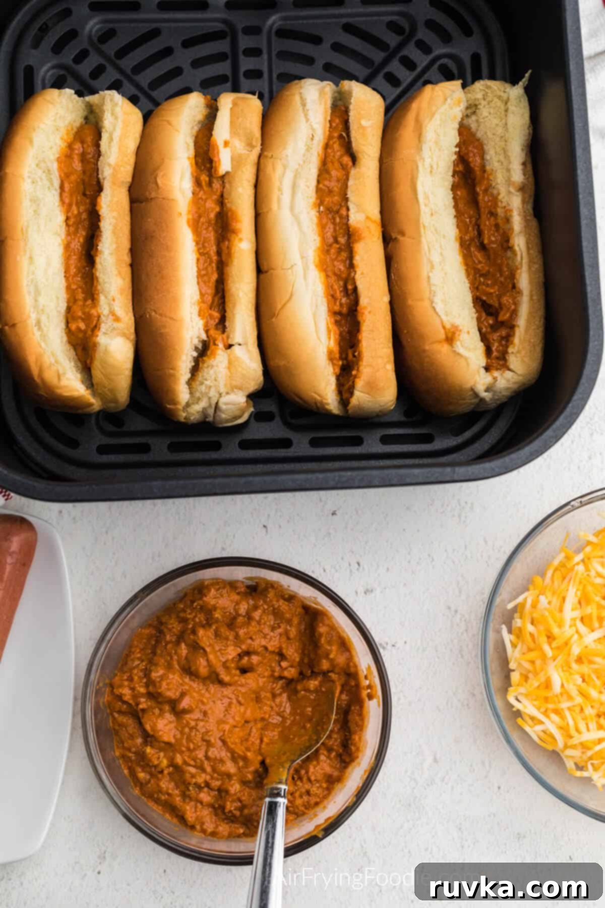 Crispy Air Fryer Chili Cheese Dogs 4 Chili scooped into the open buns in the air fryer basket, ready for hot dogs.