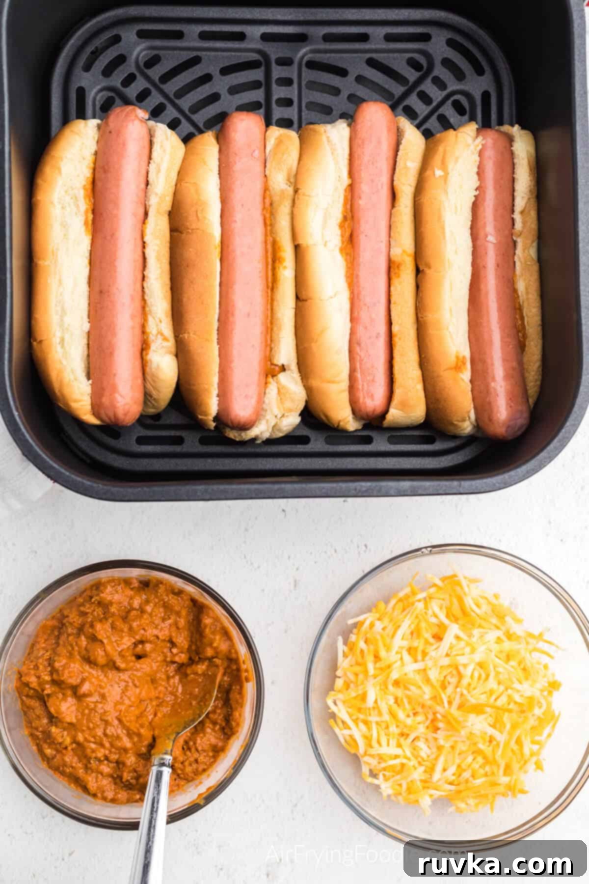 Crispy Air Fryer Chili Cheese Dogs 5 Hot dogs added to the buns with chili in the air fryer basket, showing the assembly process.