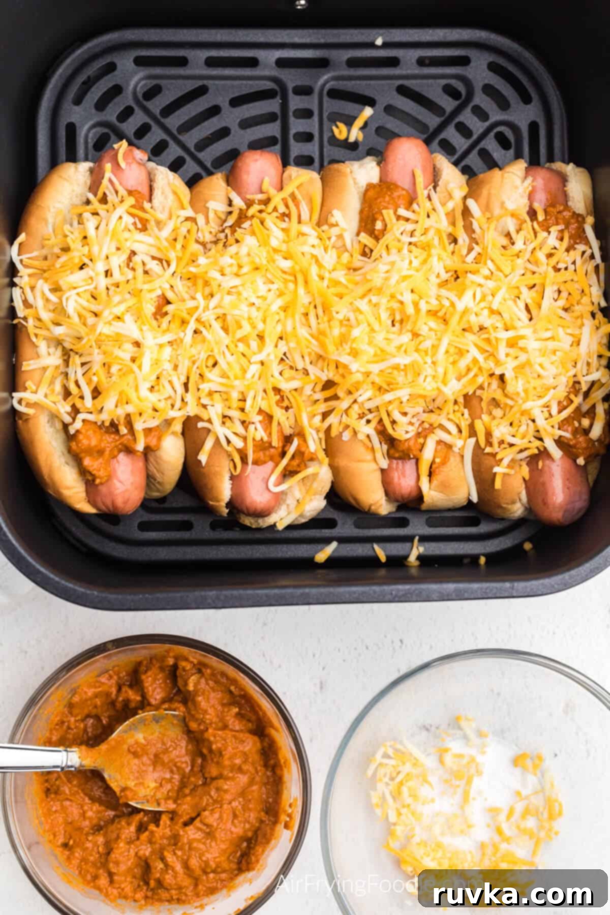 Crispy Air Fryer Chili Cheese Dogs 6 Hot dogs topped with chili and cheese in the air fryer basket, ready to be air fried to perfection.